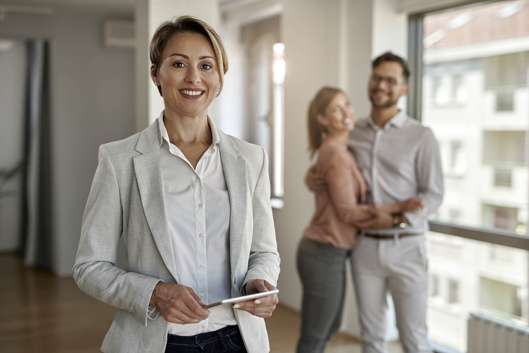 Portrait of happy real estate agent with a couple in the background.
